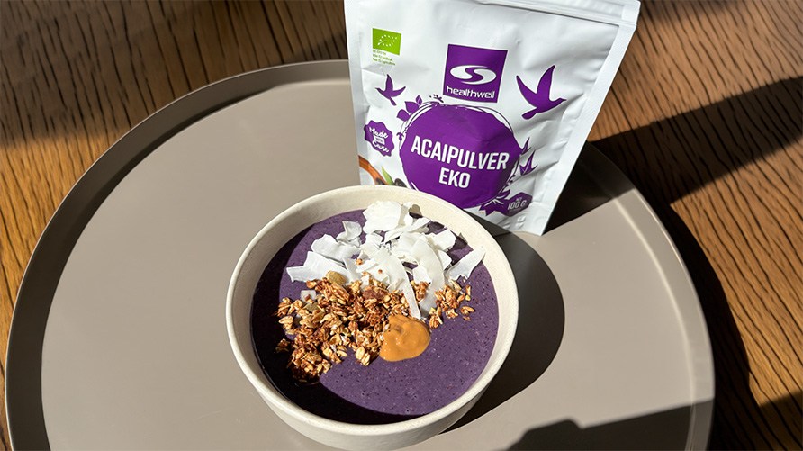 En acaibowl toppad med granola, n�tsm�r och kokosflingor p� en bricka tillsammans med Healthwell Acaipulver EKO.