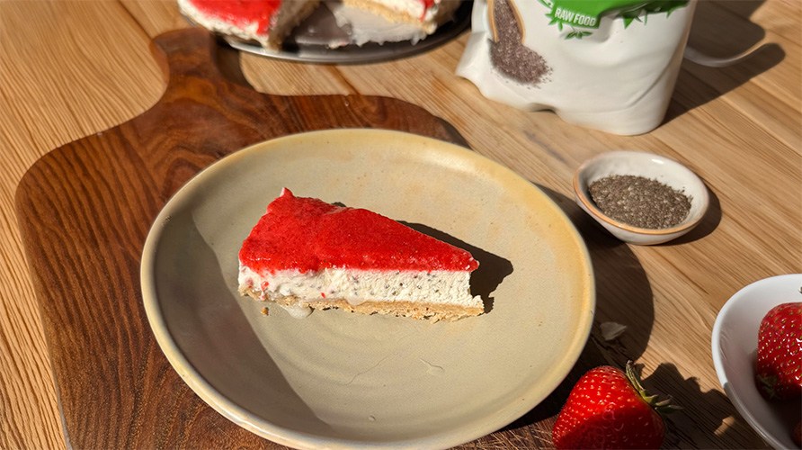 En bit chiacheesecake med jordgubbar p� en tallrik som st�r p� en tr�bricka tillsammans med en liten sk�l chiafr�n.