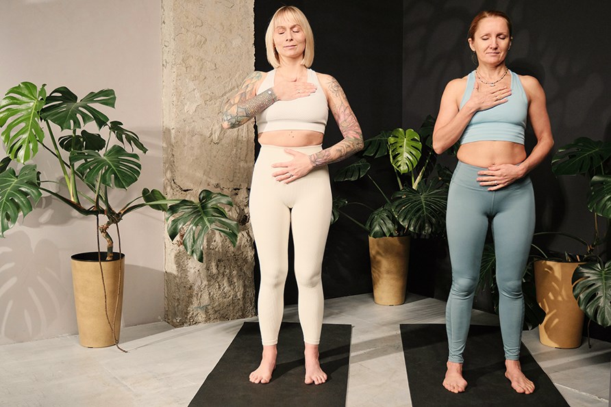 Tv� avslappnade, n�jda kvinnor utf�r andnings�vningar i en yogastudio st�endes p� yogamattor.