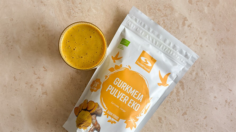 En p�se Healthwell Gurkmeja Pulver EKO p� ett bord tillsammans med ett glas gurkmejasmoothie.