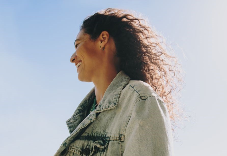 Leende kvinna ikldd jeansjacka utomhus.