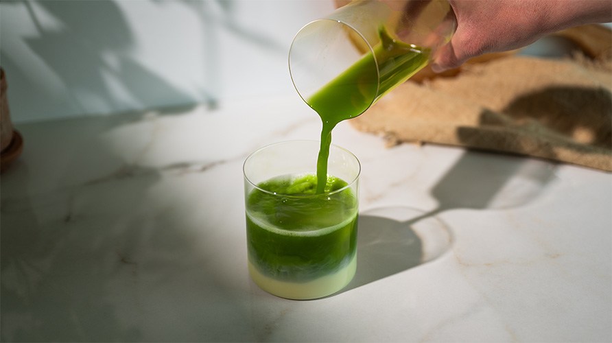 Person h�ller matcha i ett glas med mj�lk, is och mixad mango