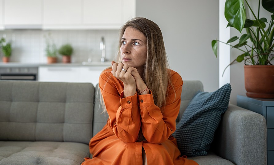 En kvinna sitter p en soffa med huvudet i hnderna och tittar ut i luften.