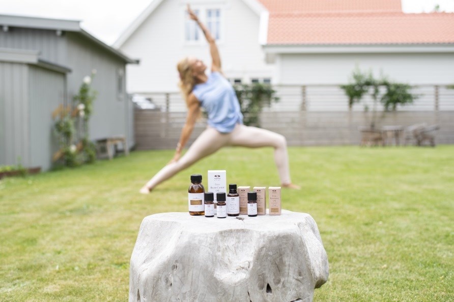 Johanna Hector i en yogaposition utomhus, framför henne står eteriska oljor uppställda på en sten.