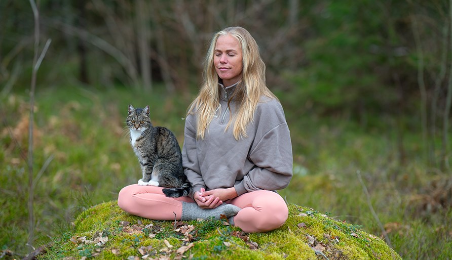Josefine sitter p en sten och mediterar med en katt i knt.