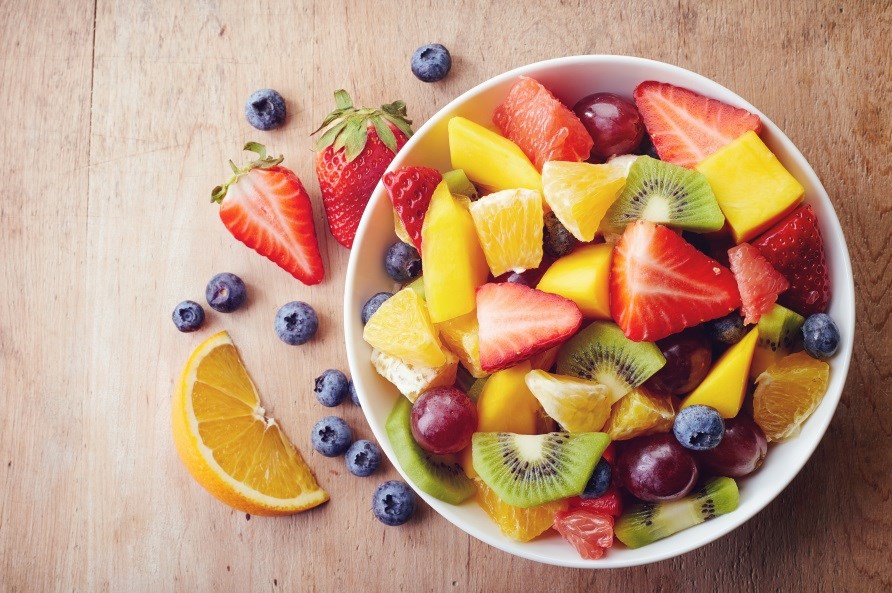 Frukter som kiwi, jordgubbar och apelsiner i bitar i en skål med blåbär bredvid.