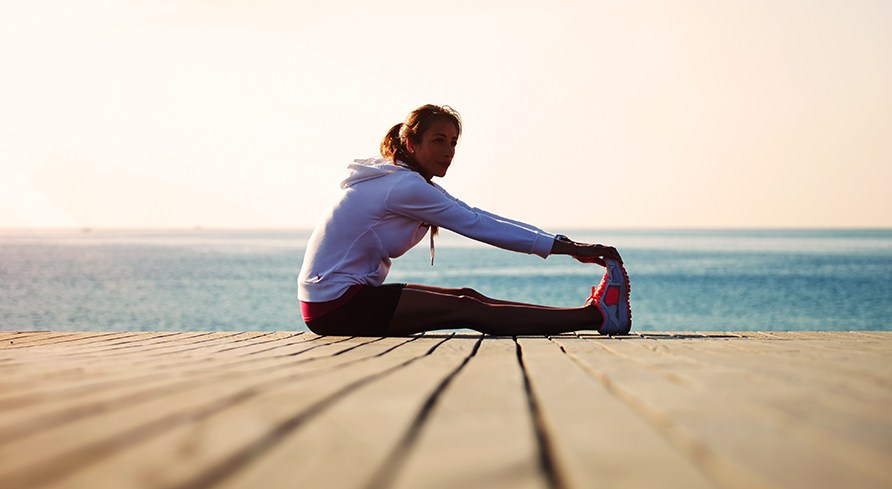 En tjej sitter p en brygga och stretchar.