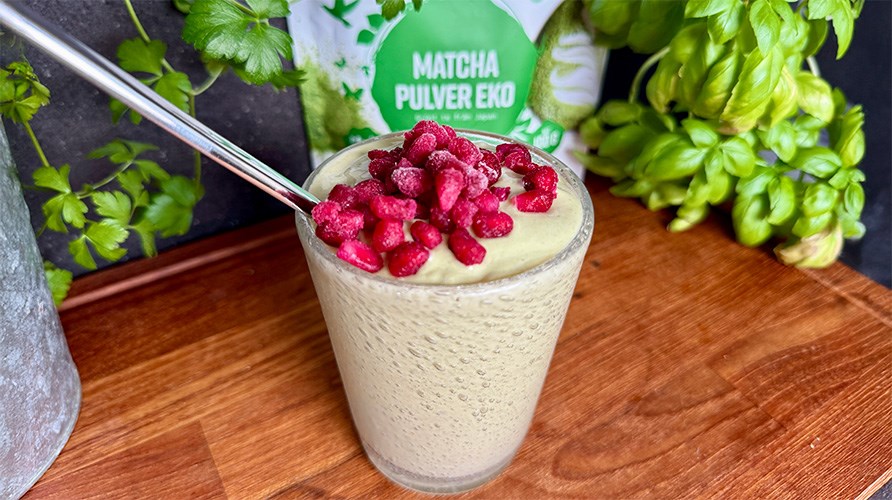 Healthwell Matcha Pulver EKO i originalfrpackning, Kalorismarts matchasmoothie i ett glas toppad med br, kruka och basilika p ett trbord. 