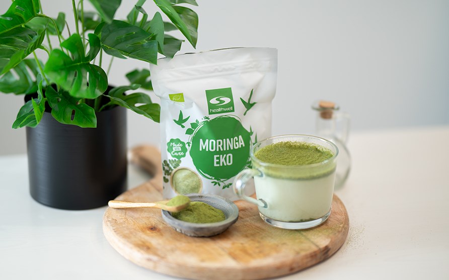 En trbricka med en kopp moringalatte p tillsammans med en pse Healthwell Moringa EKO.