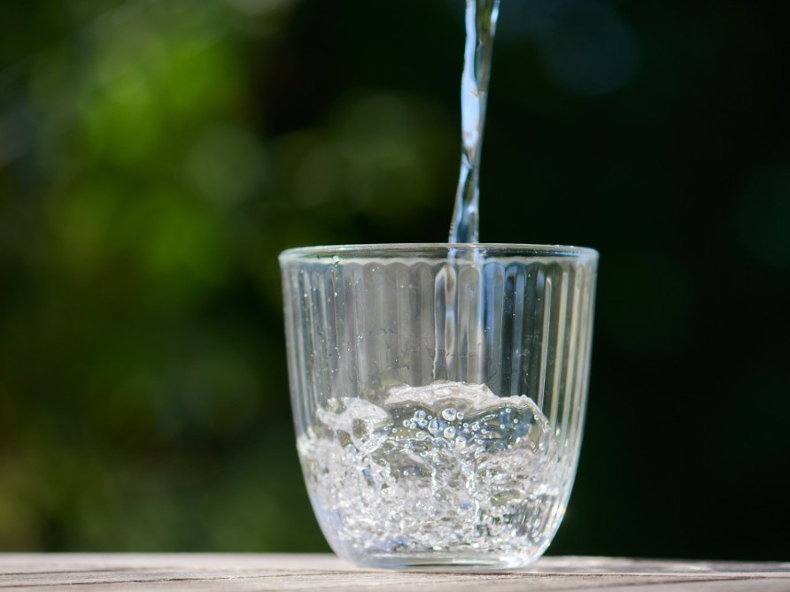 Ett glas vatten som fylls p mot en grn bakgrund. 