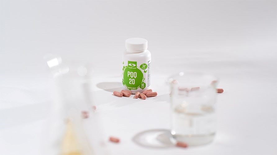 Burk med Healthwell PQQ samt kapslar av Healthwell PQQ p ett vitt bord, med med en vit bakgrund, samt med mtglas.