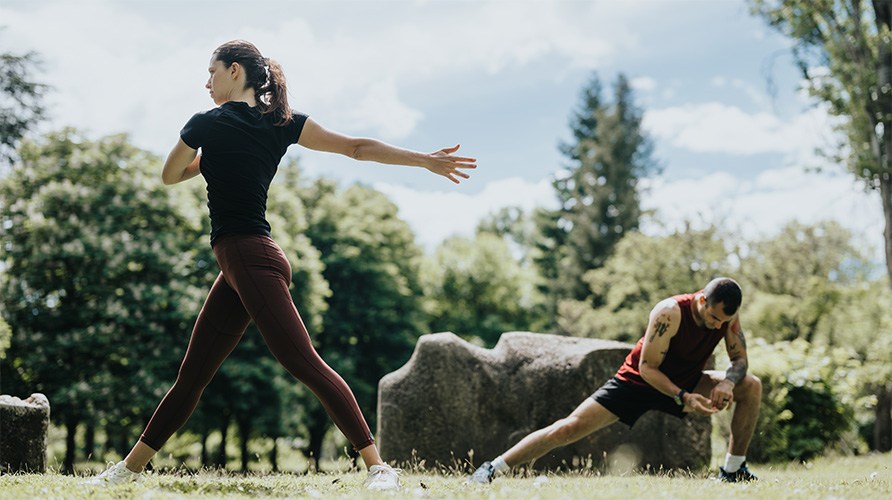 Kvinna och man stretchar i en park.