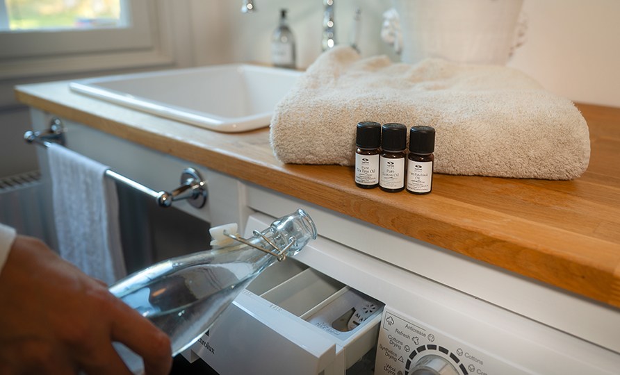 Kvinna som häller egengjort sköljmedel ur en glasflaska ner i sköljmedelsfacket på tvättmaskinen. Kvinna som häller egengjort sköljmedel ur en glasflaska ner i sköljmedelsfacket på tvättmaskinen.