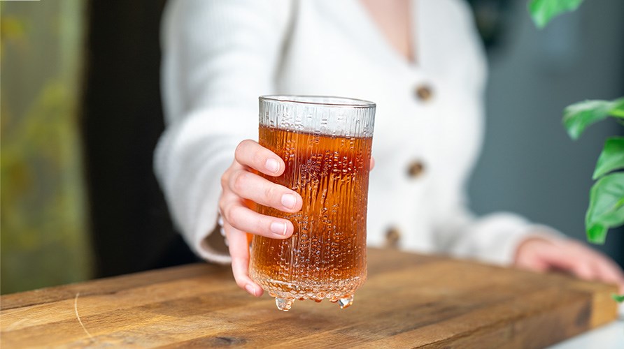 En hand som hller i ett glas med en orange dryck. 