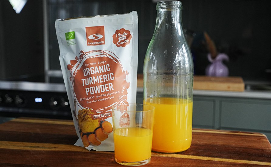 Sofia Sthls ingefrsshots i en tillbringare och i ett glas, samt Healthwell Gurkmeja Pulver EKO framdukade p en kksbnk.