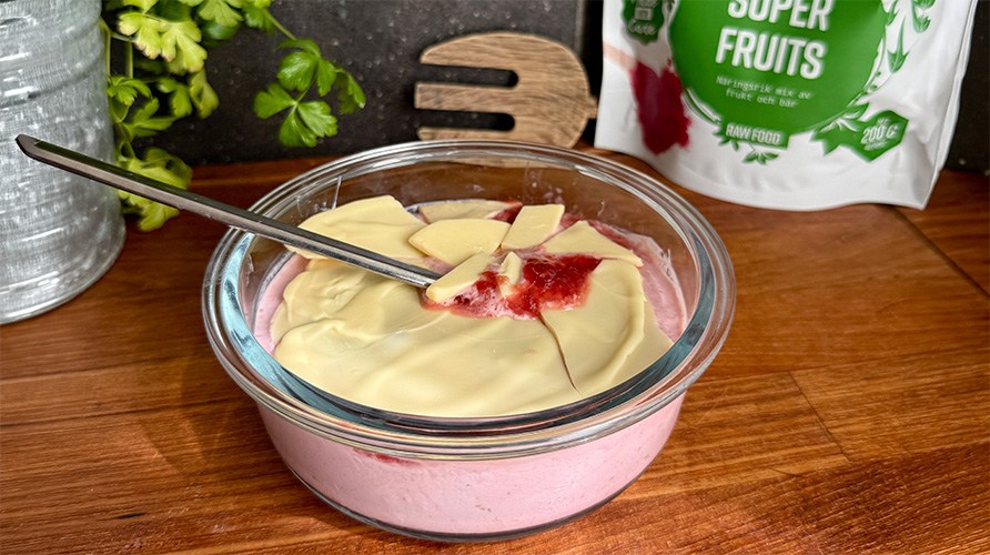 En sk�l med jordgubbskvarg toppad med jordgubbssylt och sm�lt vit choklad, med ett paket Healthwell Super Fruits i bakgrunden.