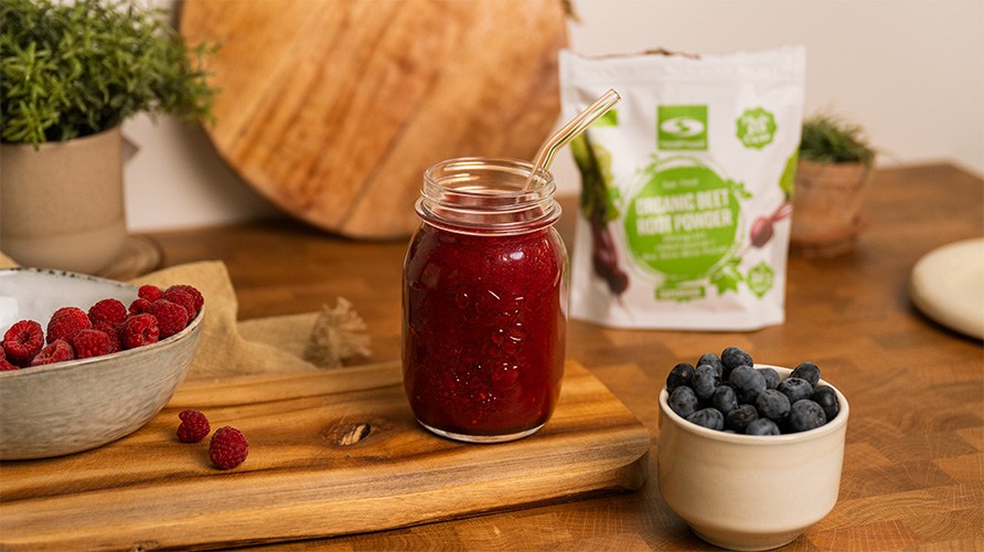 Smoothie med hallon och bl�b�r i ett glas som st�r p� en tr�bricka p� ett bord med en p�se Healthwell R�dbetspulver EKO i bakgrunden
