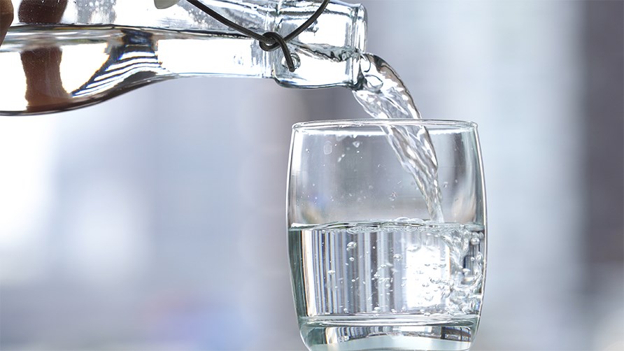 Vatten från glasflaska hälls upp i ett glas.